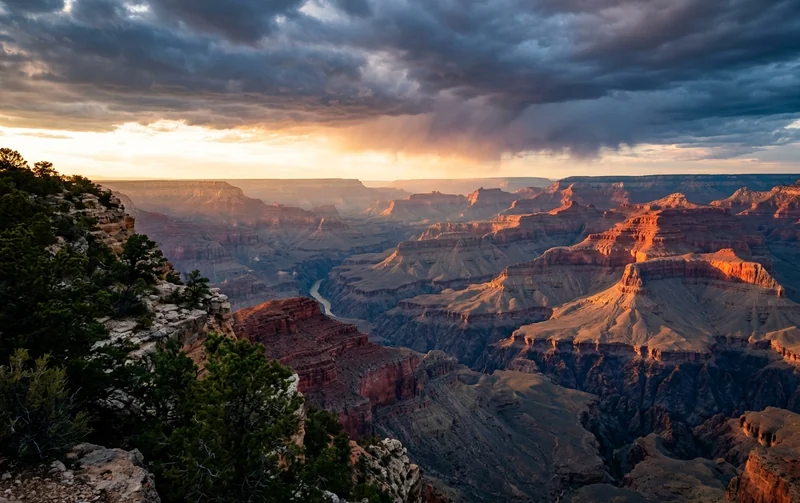 Grand Canyon buttes glowing orange at sunset under dark storm clouds from the South Rim