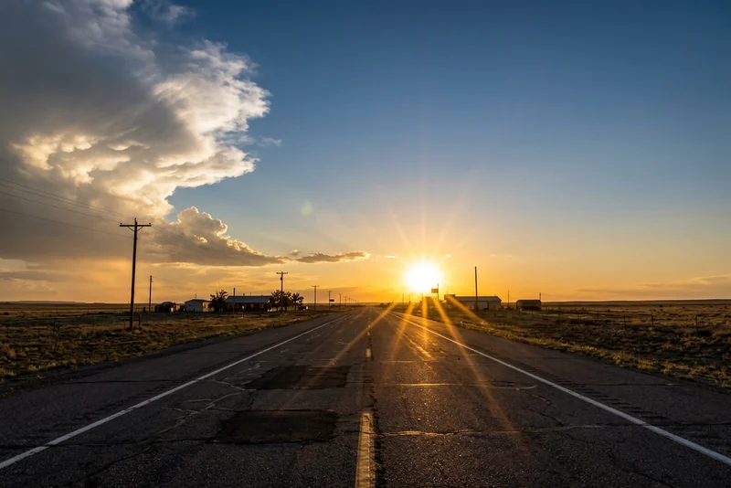 Sun setting over the cracked two-lane Route 66 near Joseph City, Arizona, under storm clouds